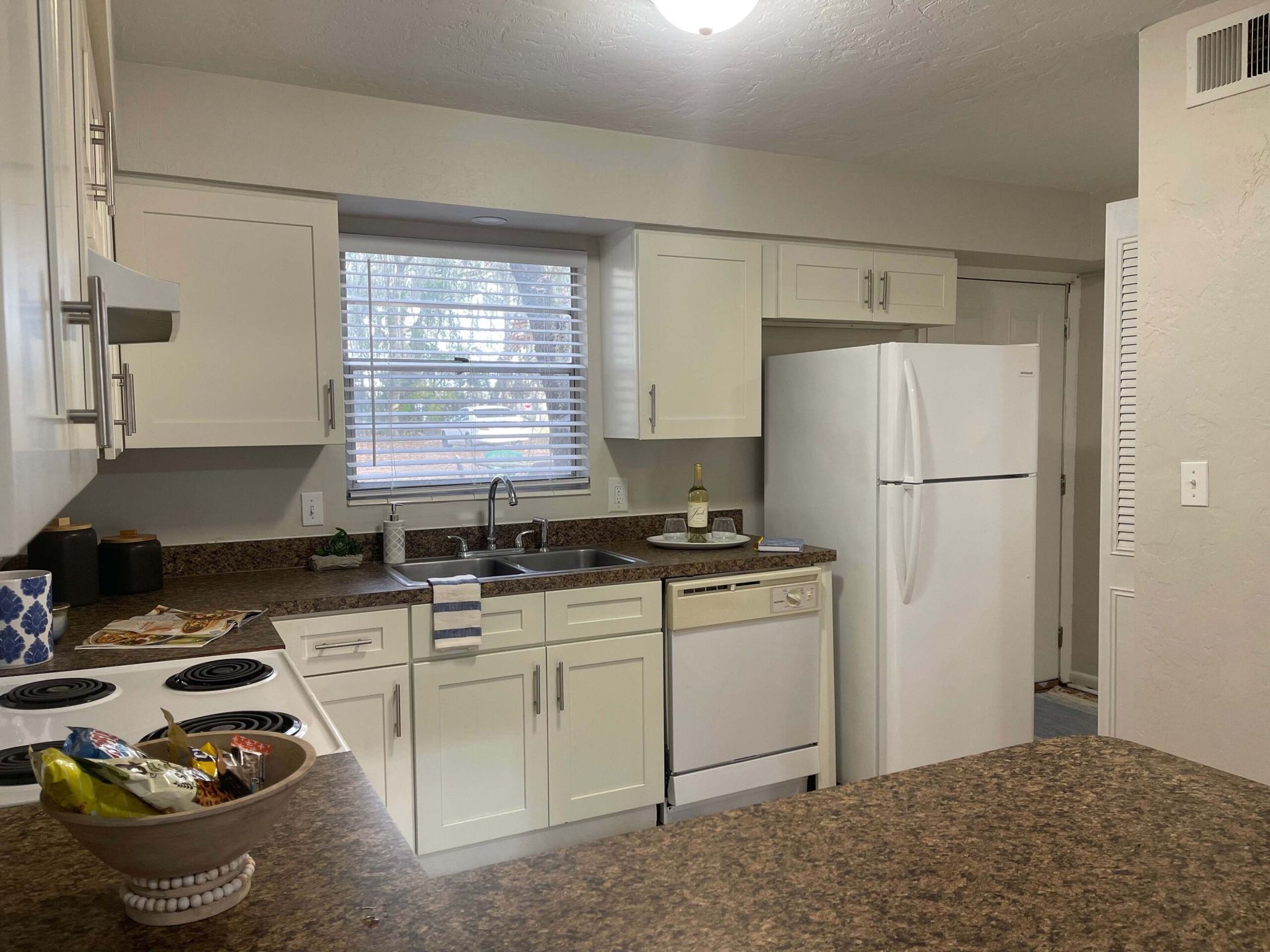 A kitchen with white cabinets , a white refrigerator , a stove , a sink , and a window.