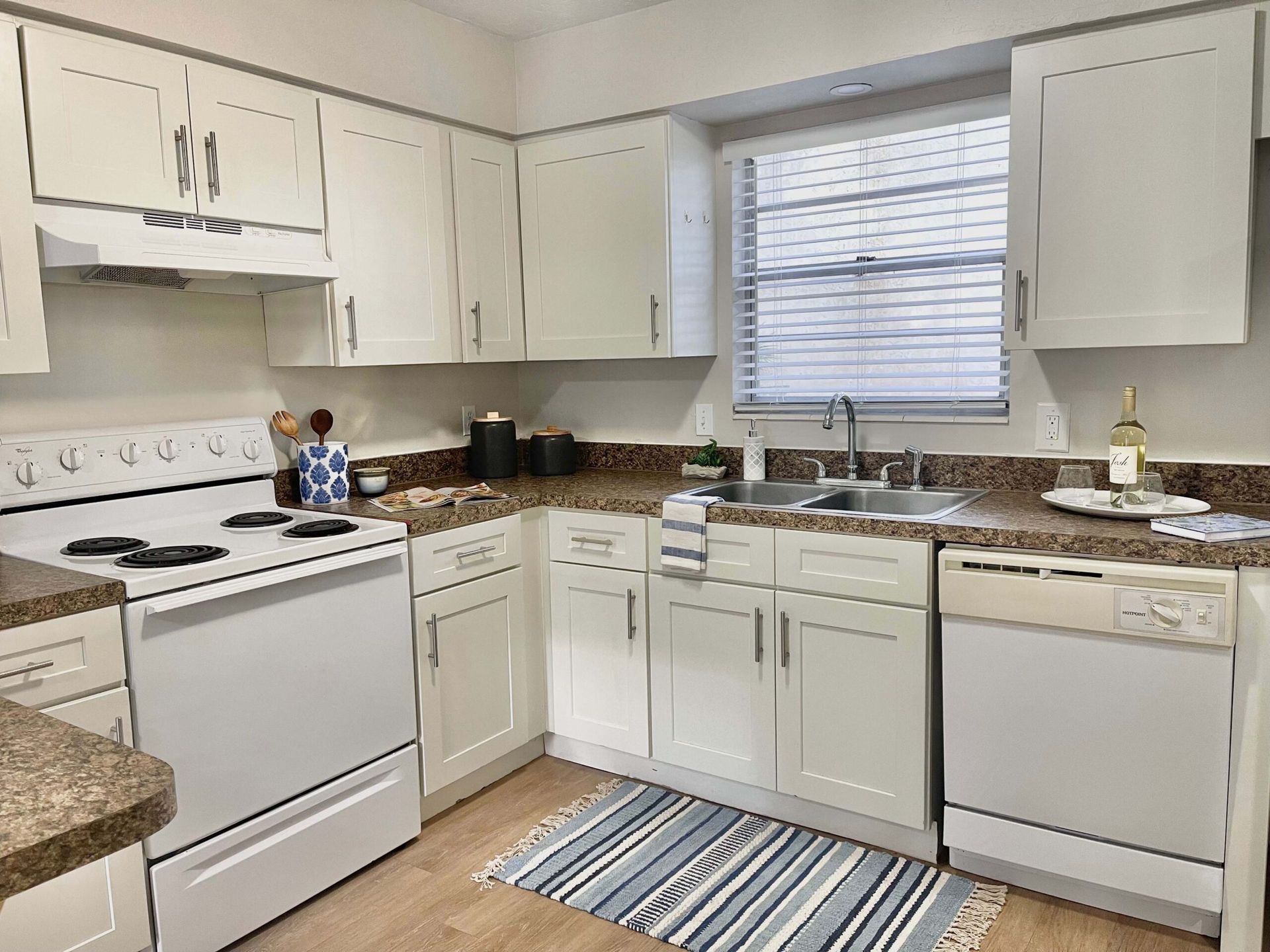 A kitchen with white cabinets , a stove , a sink , and a window.