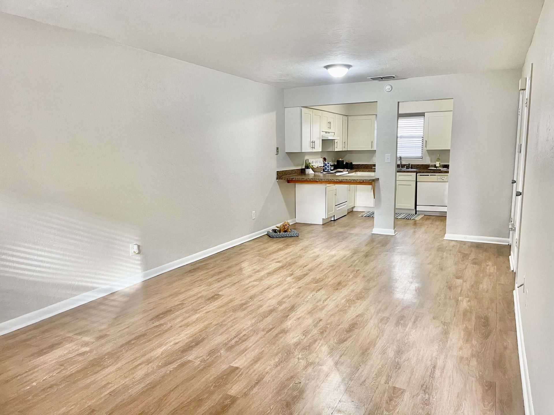 A living room with hardwood floors and a kitchen in the background.