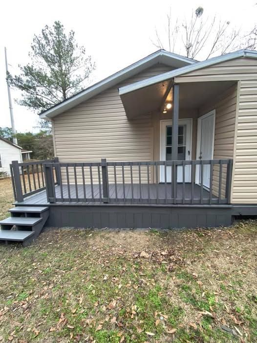 A small gray deck with steps in front of a house with tan siding and a door.