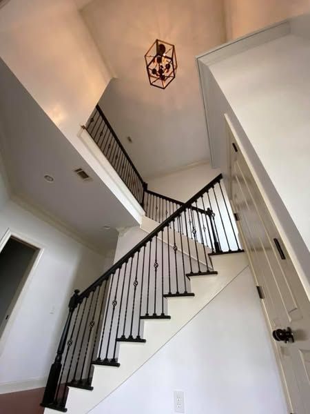 Staircase leading to a second floor with black wrought iron railing, white walls, and a dark light fixture.