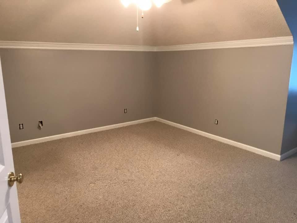 Empty room with tan carpet, gray walls, white trim, and a sloped ceiling.