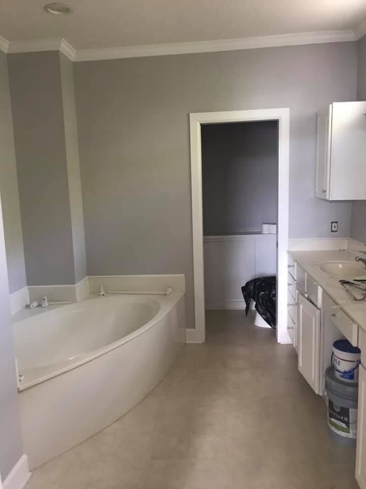 Bathroom with gray walls, white tub, cabinetry, and a doorway.