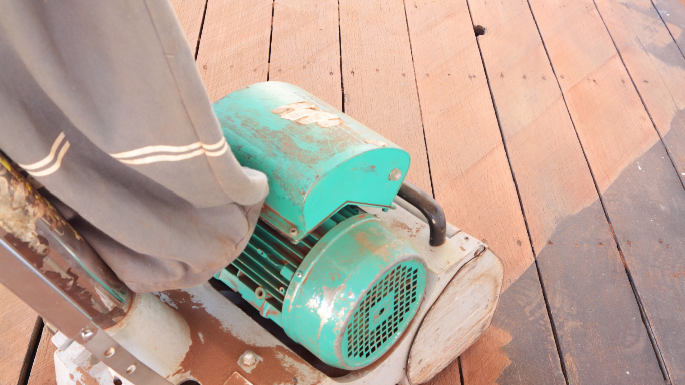Person sanding a wooden floor with a green and white electric sander.