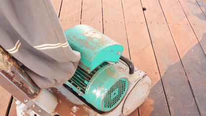 Person sanding a wooden floor with a green and white electric sander.