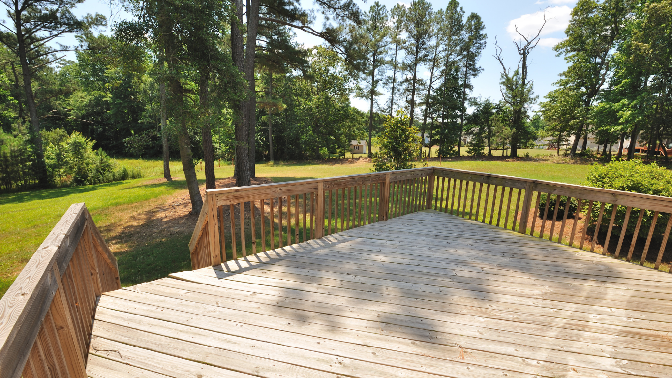 Wooden deck overlooking a sunny, grassy backyard with trees.