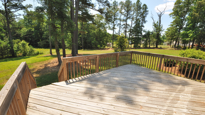 Wooden deck overlooking a sunny, grassy backyard with trees.