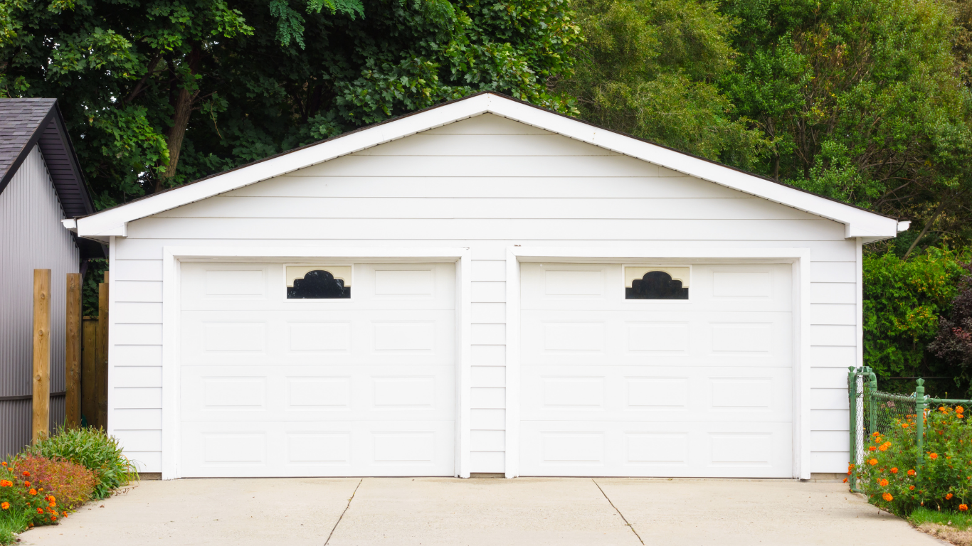 White two-car garage with arched windows, set in a residential area with green foliage.