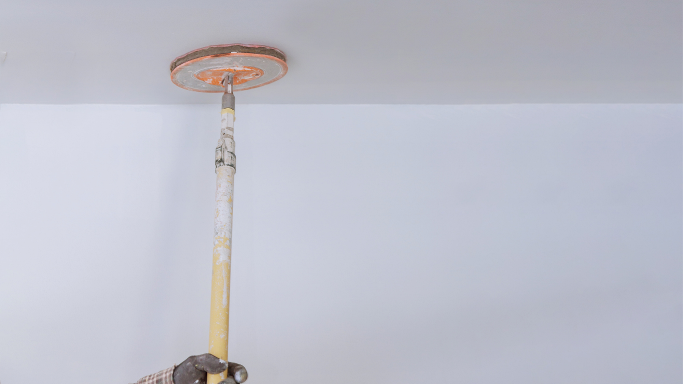 A person sands a white ceiling with a long-handled sanding tool.