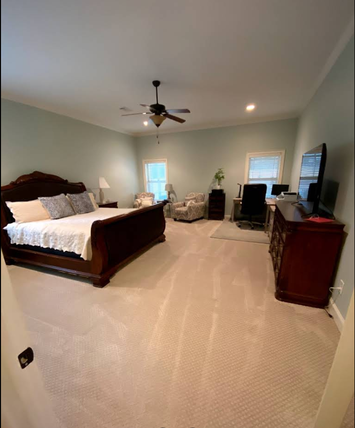 Spacious bedroom with a king-size bed, desk, sitting area, and neutral carpet. Dark wood furniture and light blue walls.