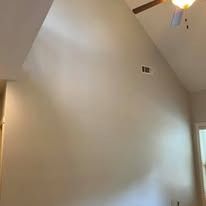Tan wall with a high ceiling, air vent, and a ceiling fan.