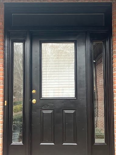 Black front door with sidelights; brick exterior.