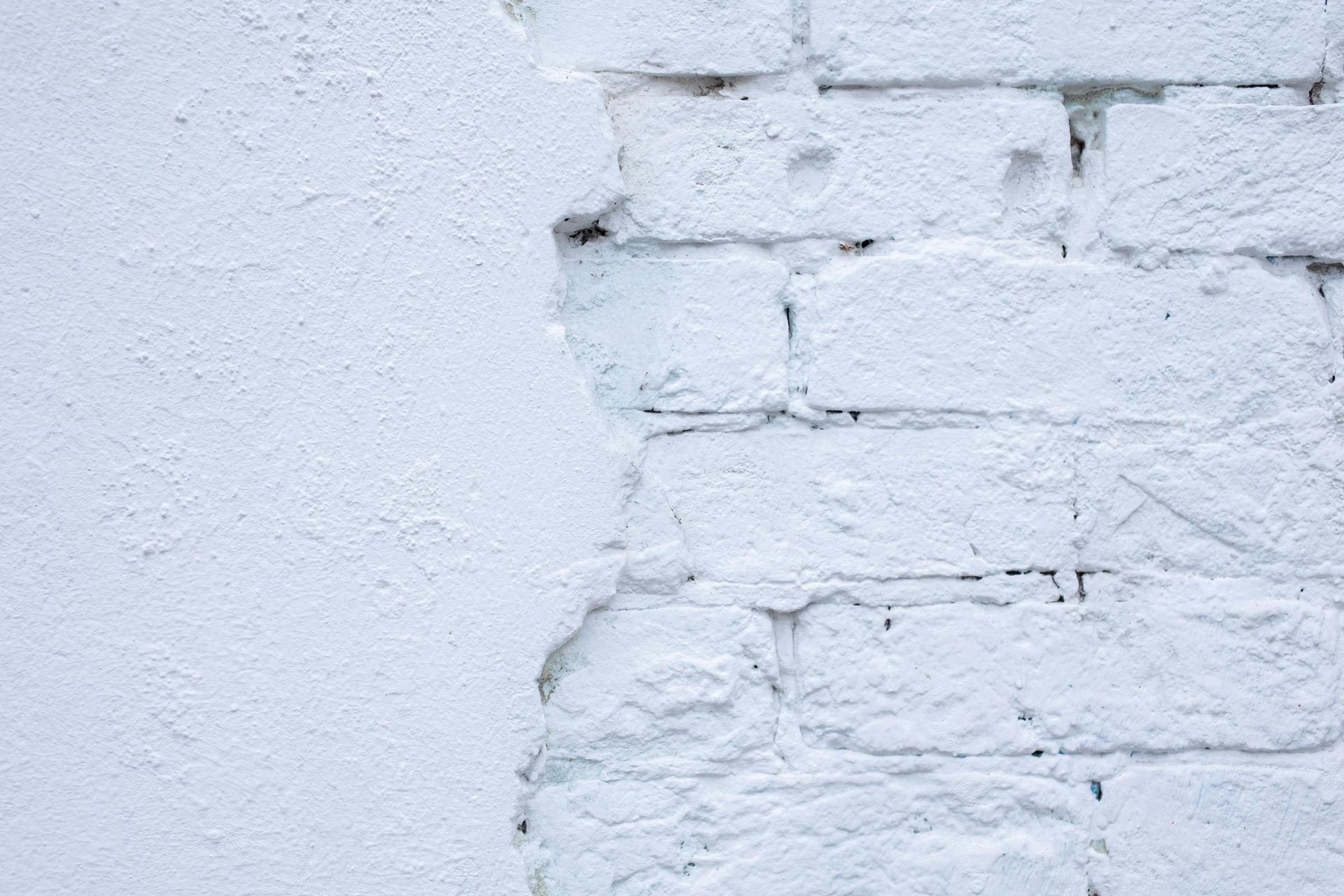 White painted brick wall with peeling paint, showing underlying bricks.