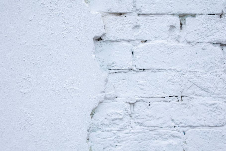 White painted brick wall with peeling paint, showing underlying bricks.
