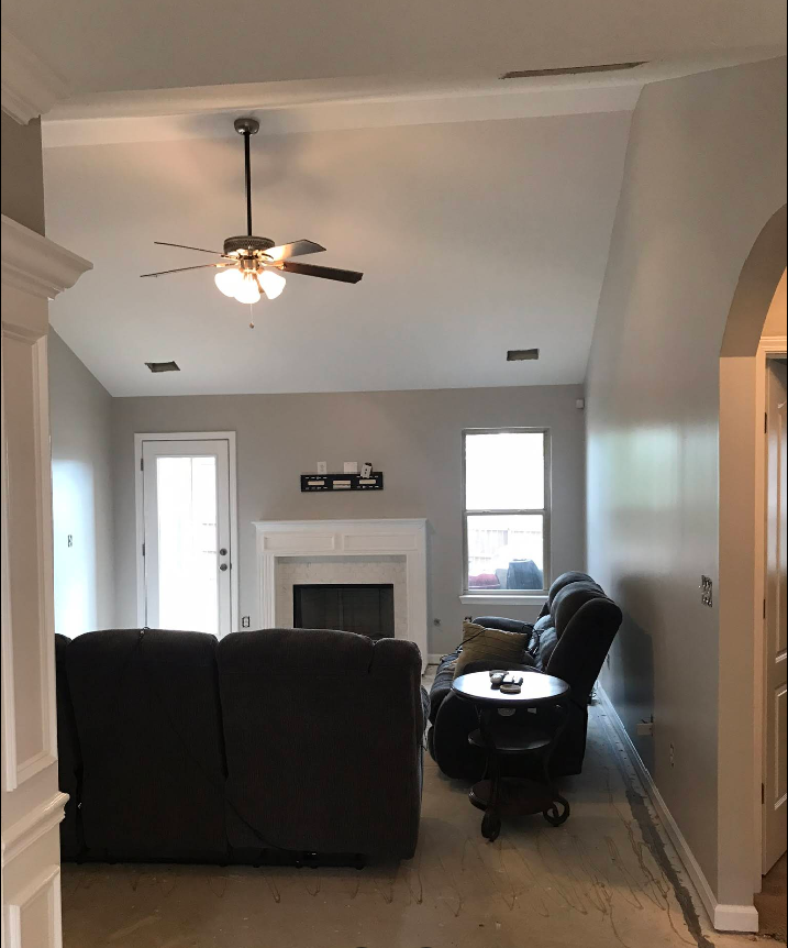Living room with gray walls, couch, fireplace, ceiling fan, and doorway to another room.