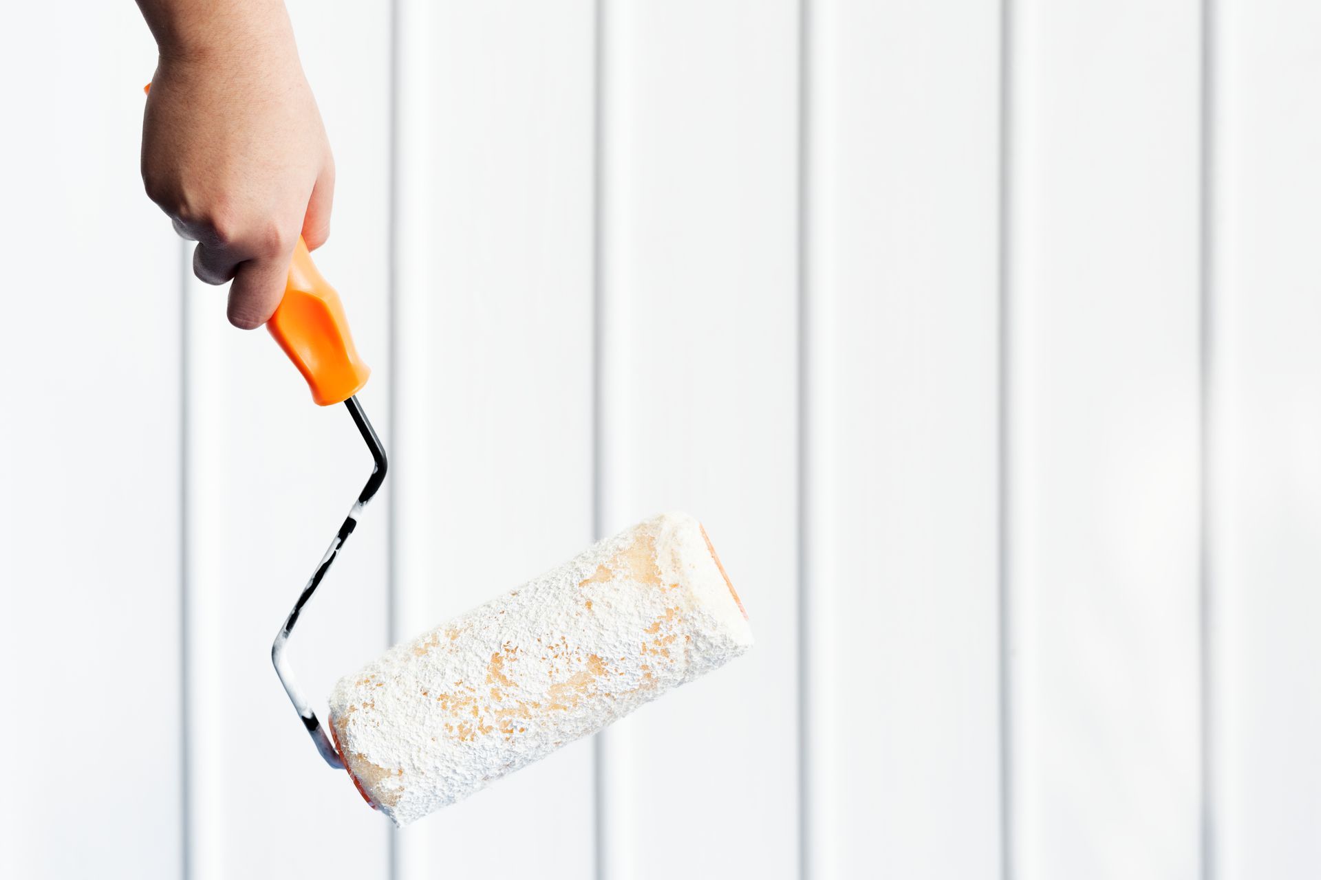 Hand holding paint roller against white vertical panels.