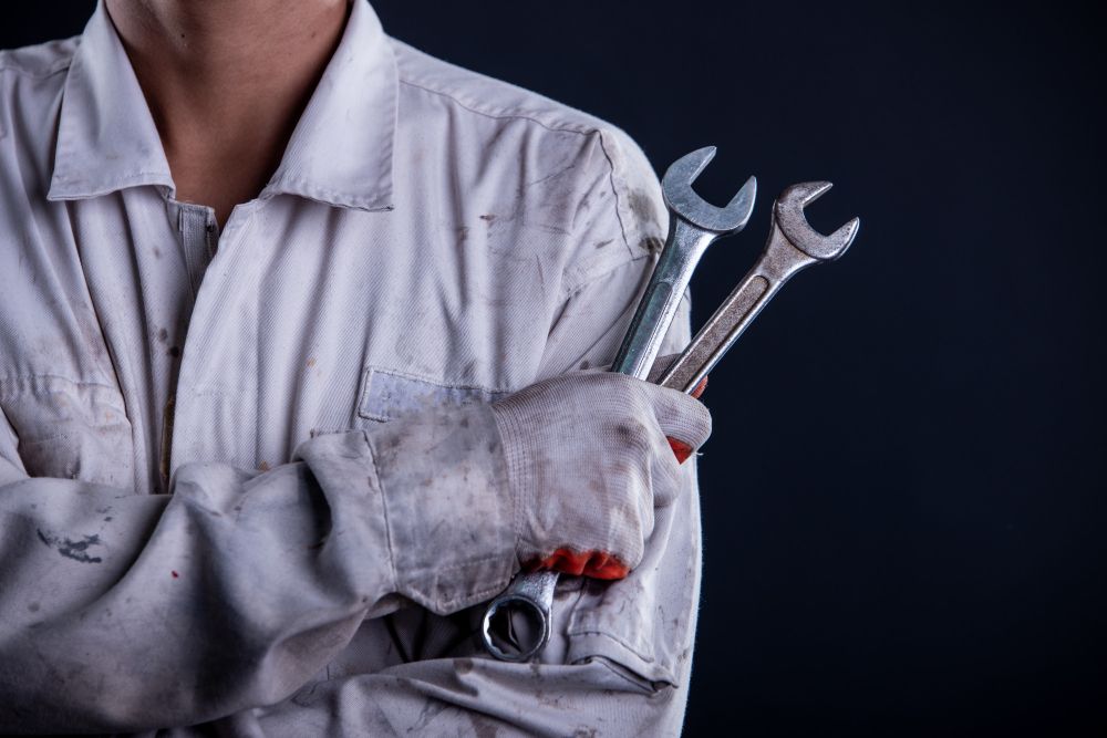 A man in a white uniform is holding three wrenches in his hands.