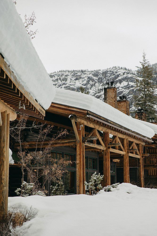 A wooden house covered in snow with a mountain in the background.