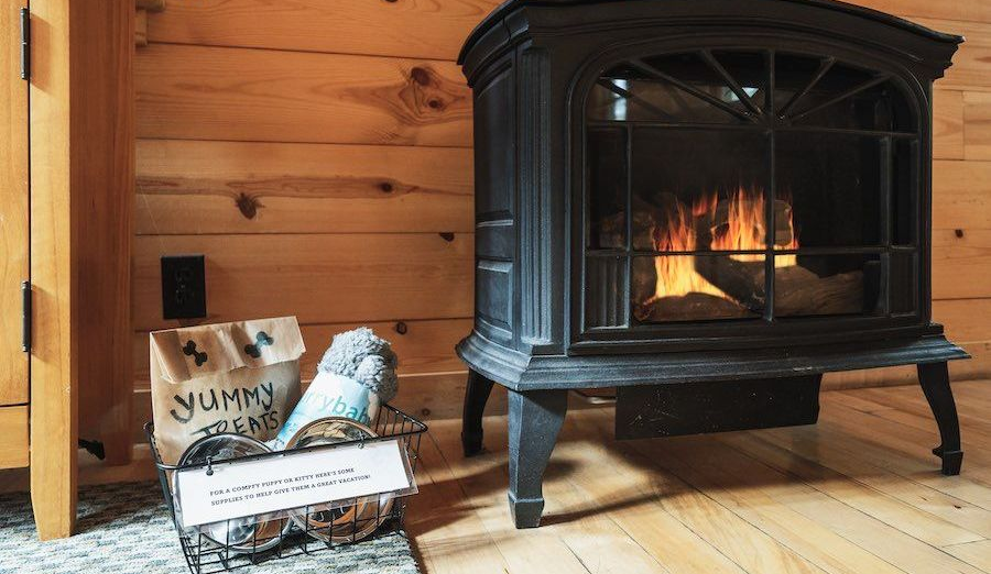 Cozy cabin corner with a black wood stove, fire inside, and a basket of firewood on a wooden floor