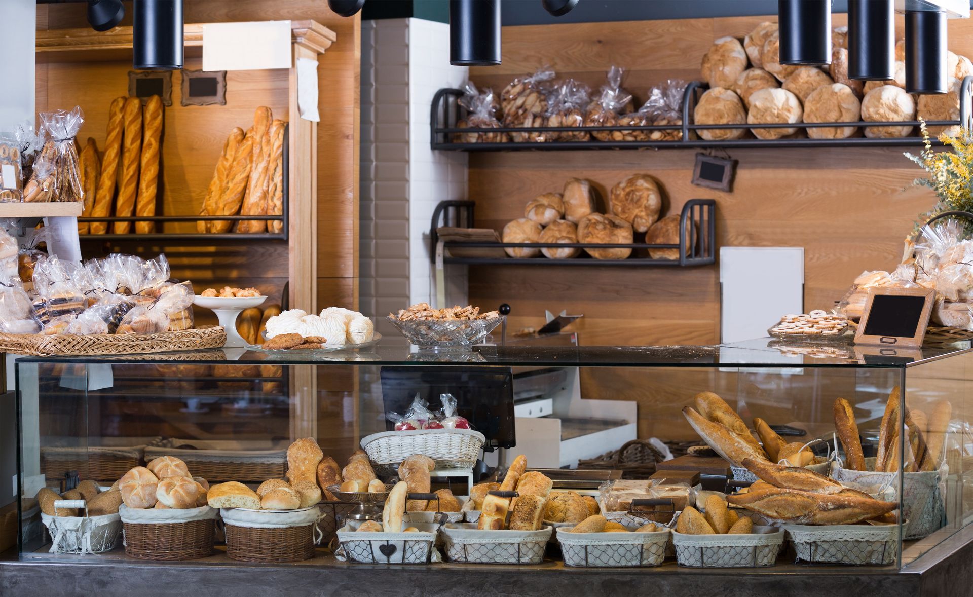 Bakery display with various breads, pastries, and baked goods in baskets and shelves. Wooden backdrop.