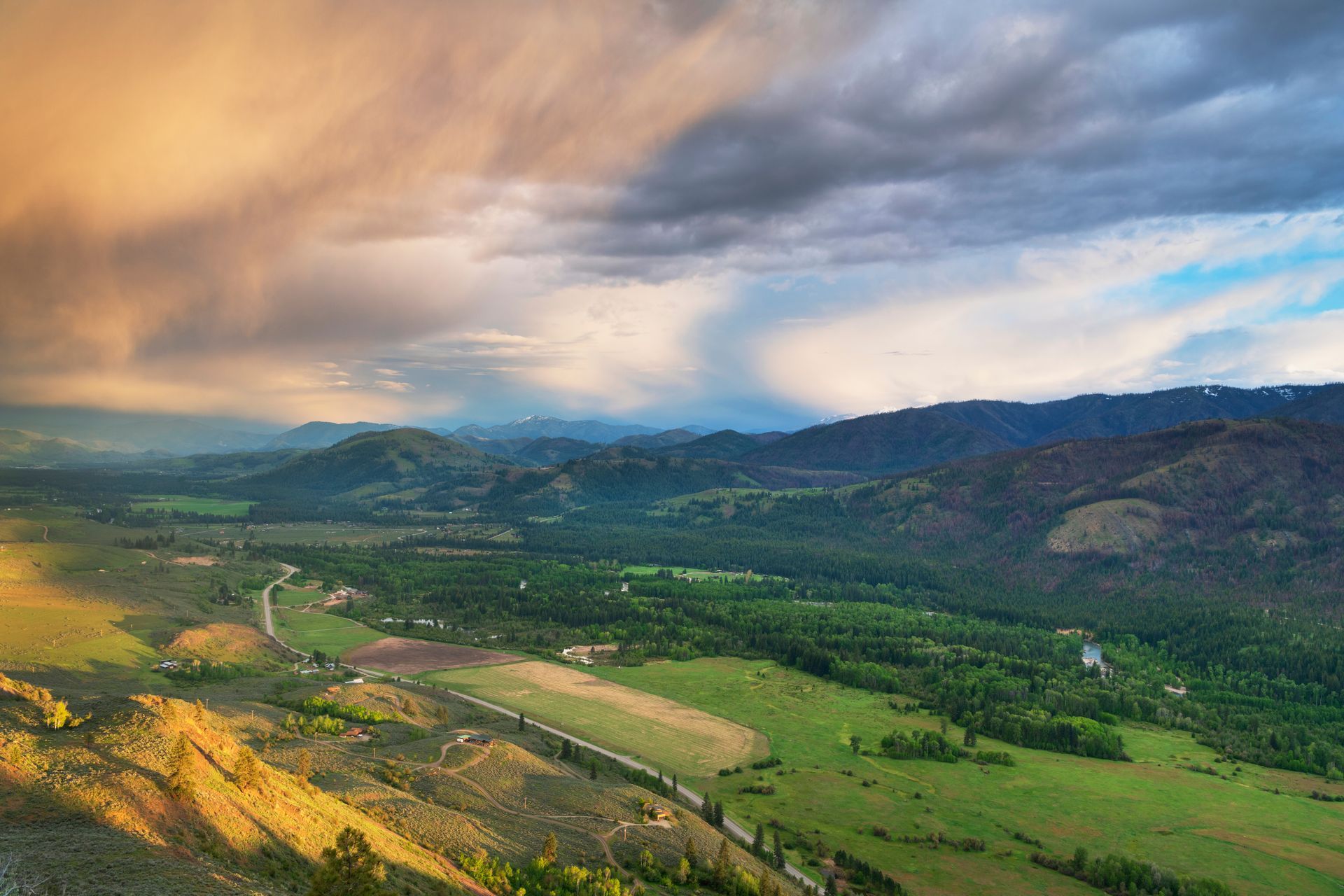 Rolling green valley under a dramatic sky with golden light and dark clouds.