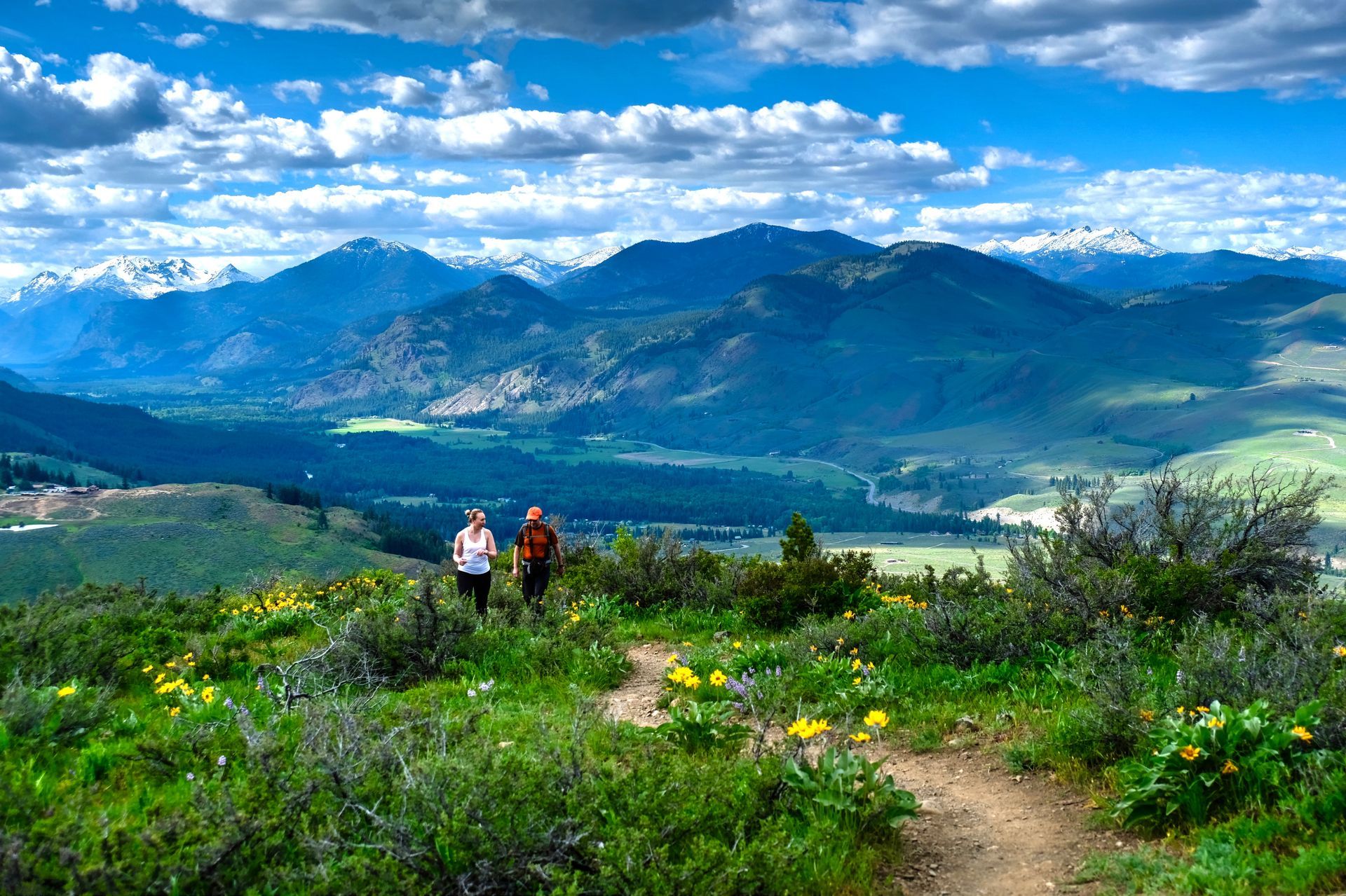 Two people are walking on a trail in the mountains.
