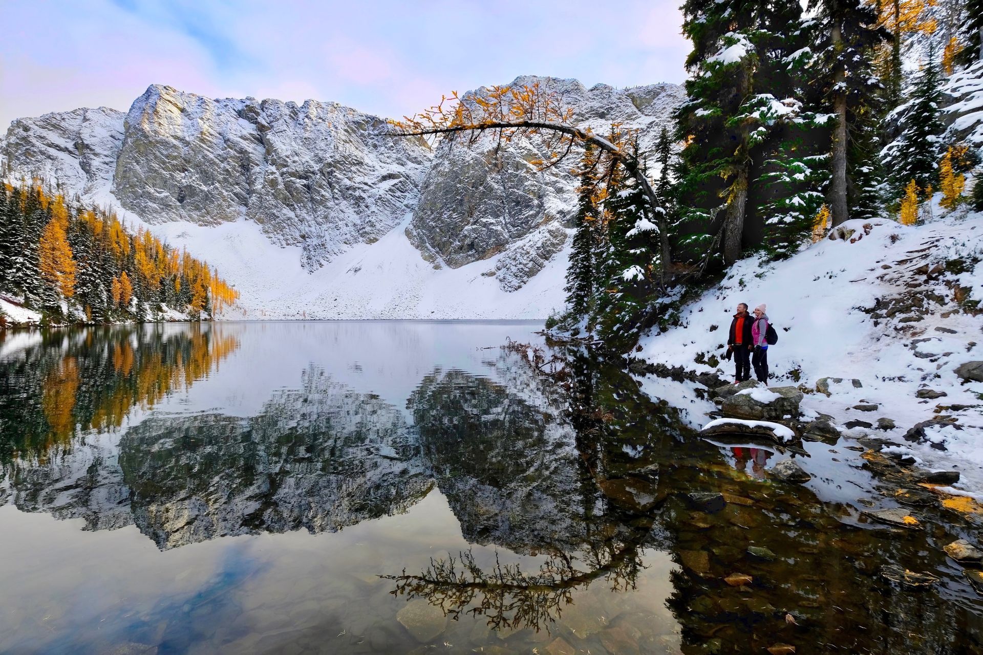 A couple standing next to a lake with mountains in the background