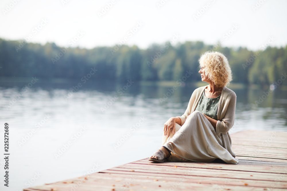 A woman is sitting on a dock near a lake.