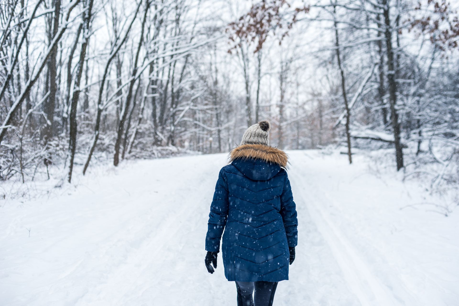 A woman is walking down a snowy path in the woods.