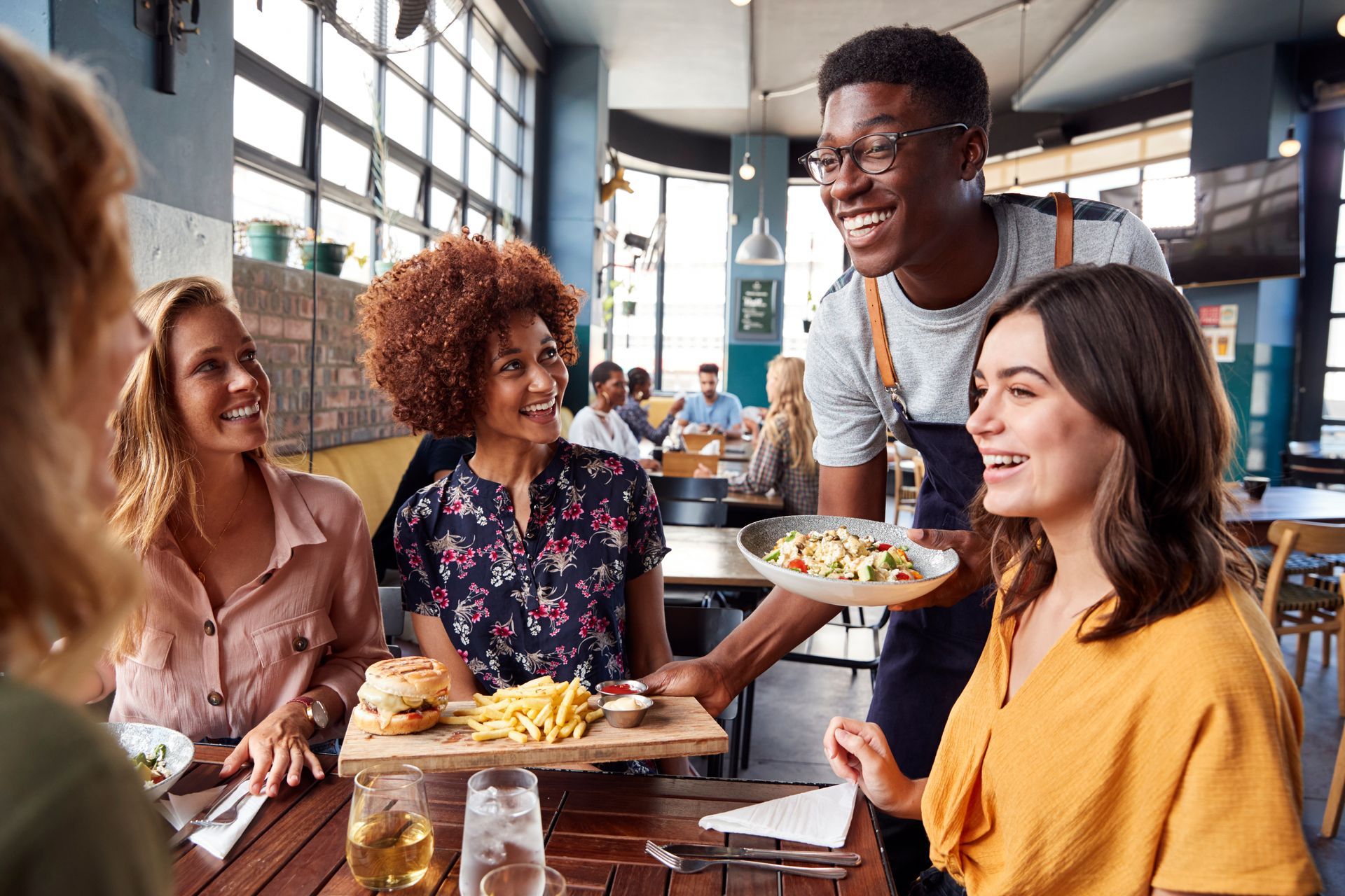 A server smiles, delivering food to a group of people at a restaurant.