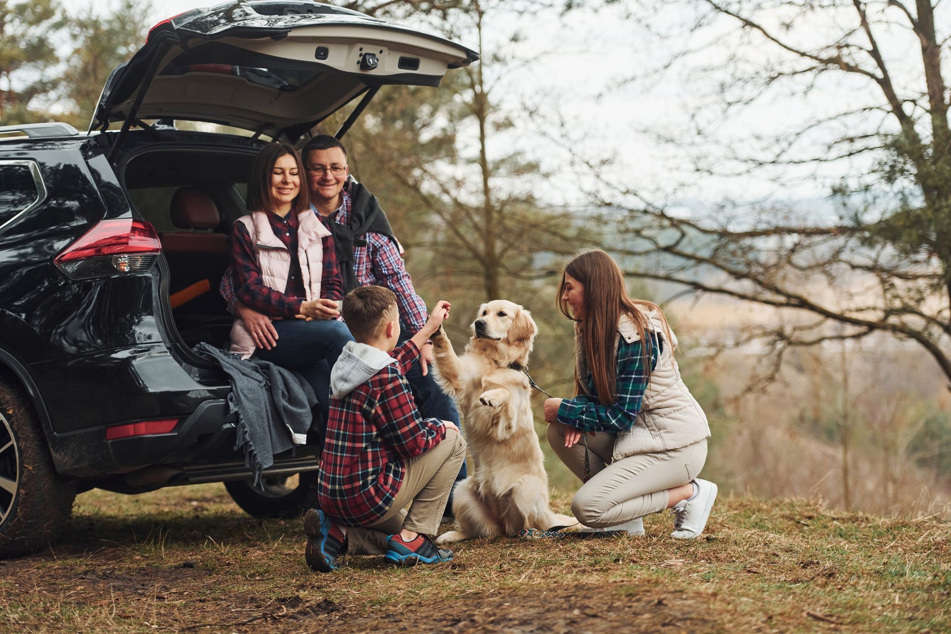 Family with two dogs outdoors by an SUV; woman petting a golden retriever.