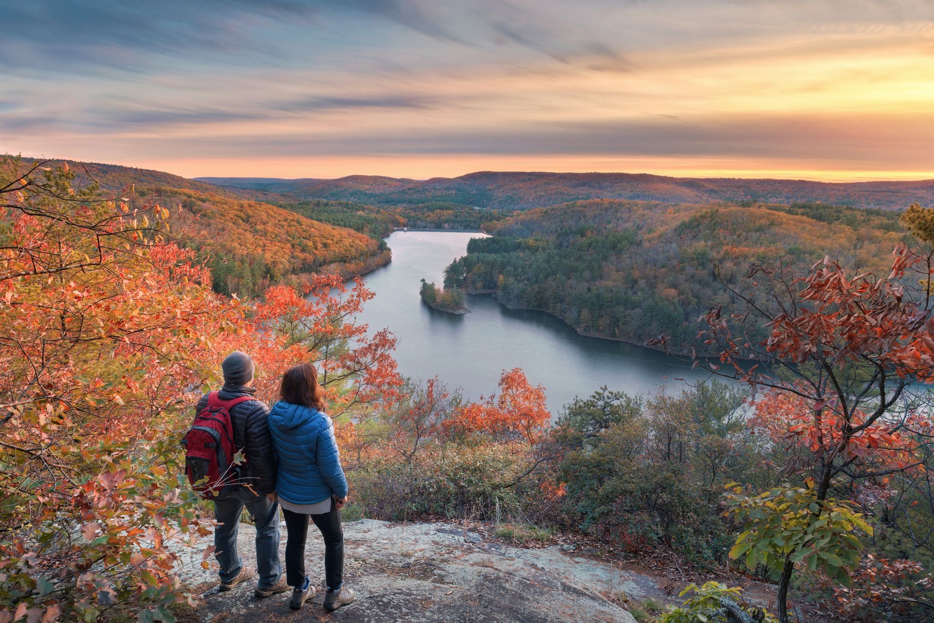 Couple overlooking a lake surrounded by autumn trees at sunset.