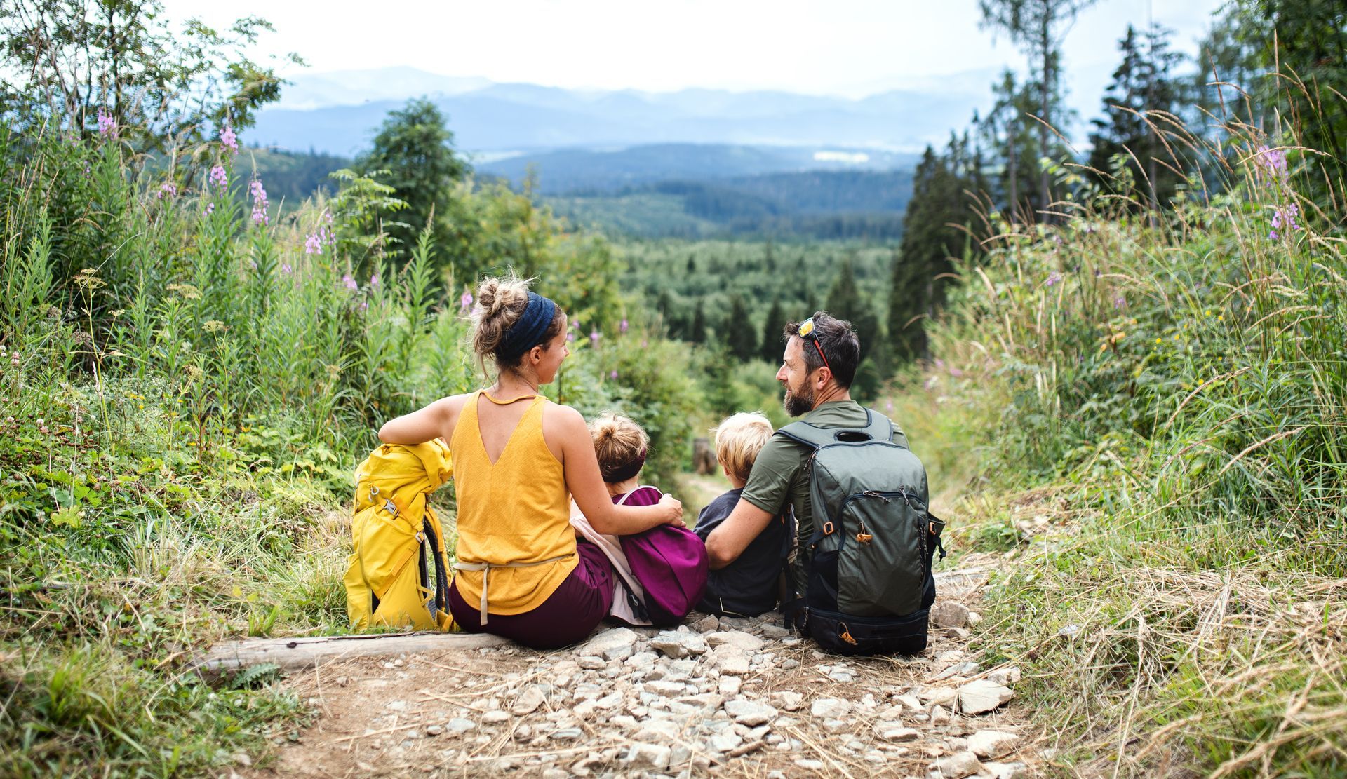 A family is sitting on the ground in the woods looking at the view.