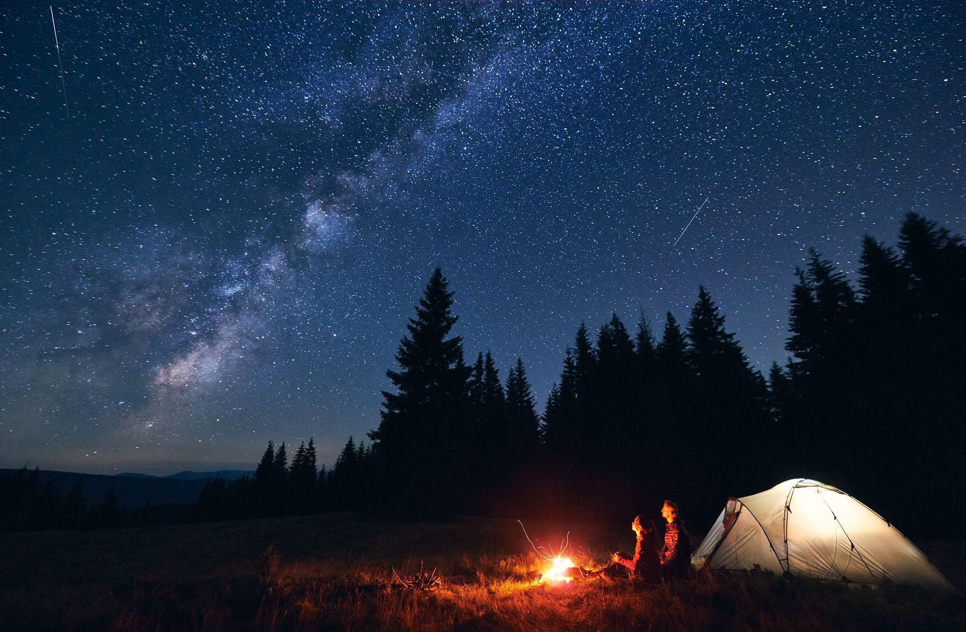 A group of people are sitting around a campfire under a starry night sky.