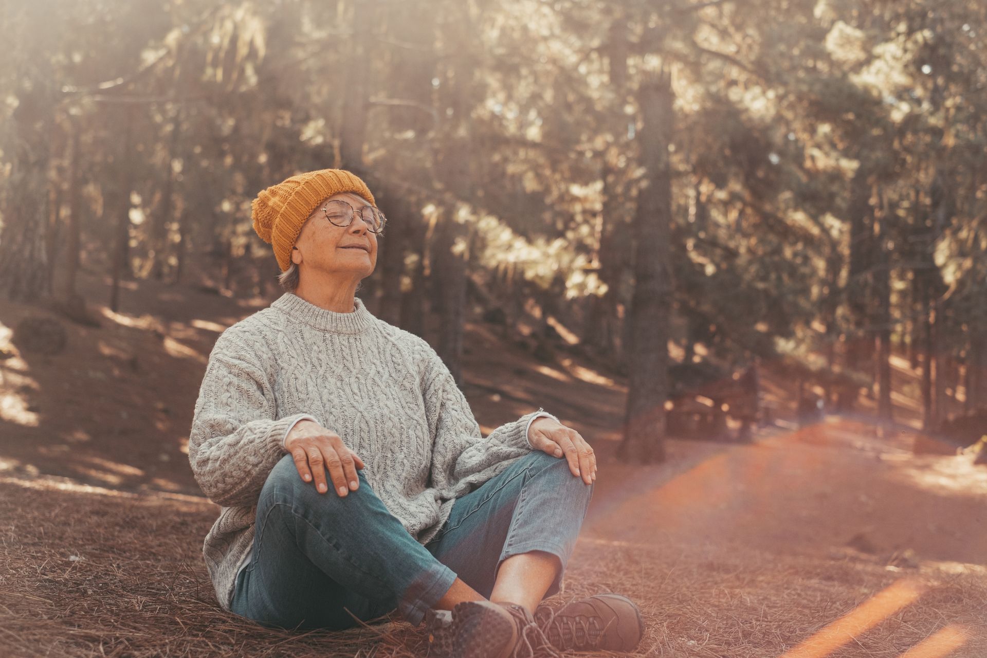 A woman is standing in the woods looking up at the sky.