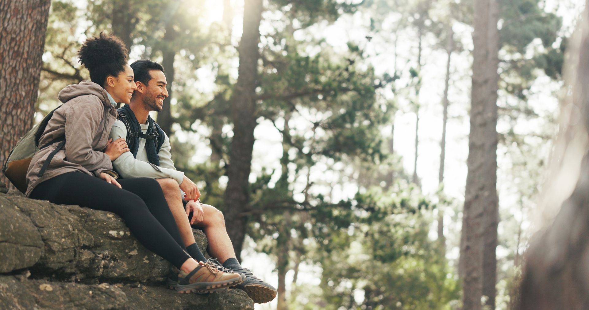 A man and a woman are sitting on a rock in the woods.