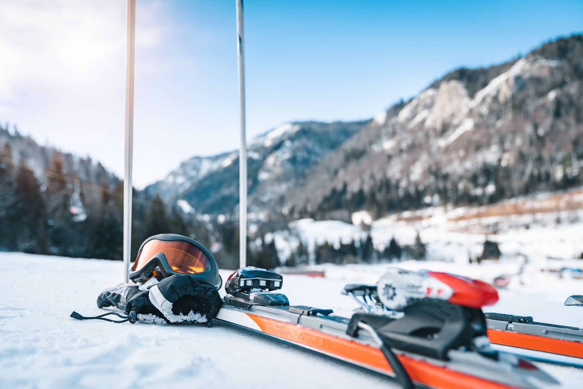 Skis and goggles on snowy ground in front of mountains and blue sky.