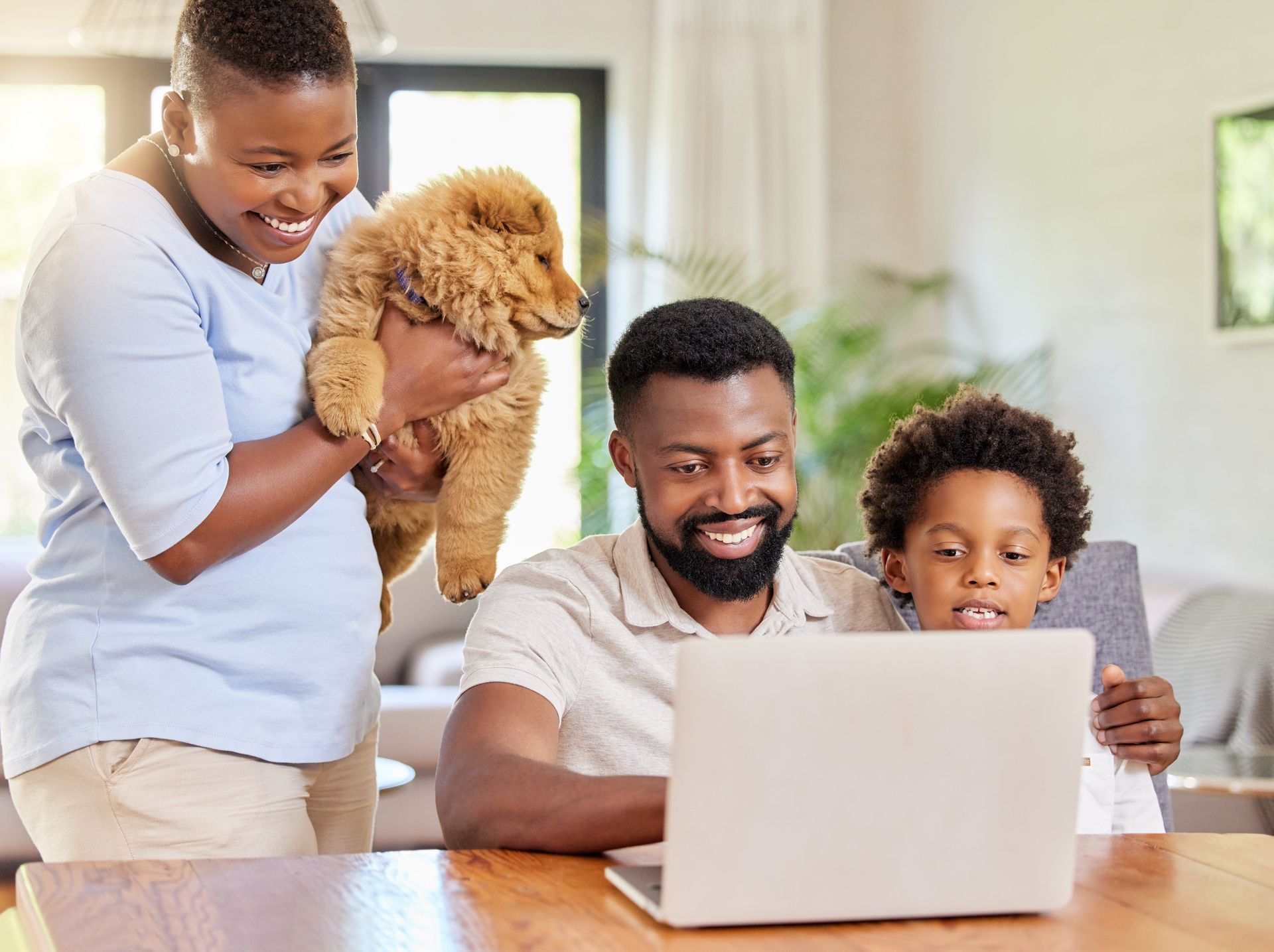 Family of four smiles at a laptop while a woman holds a puppy.