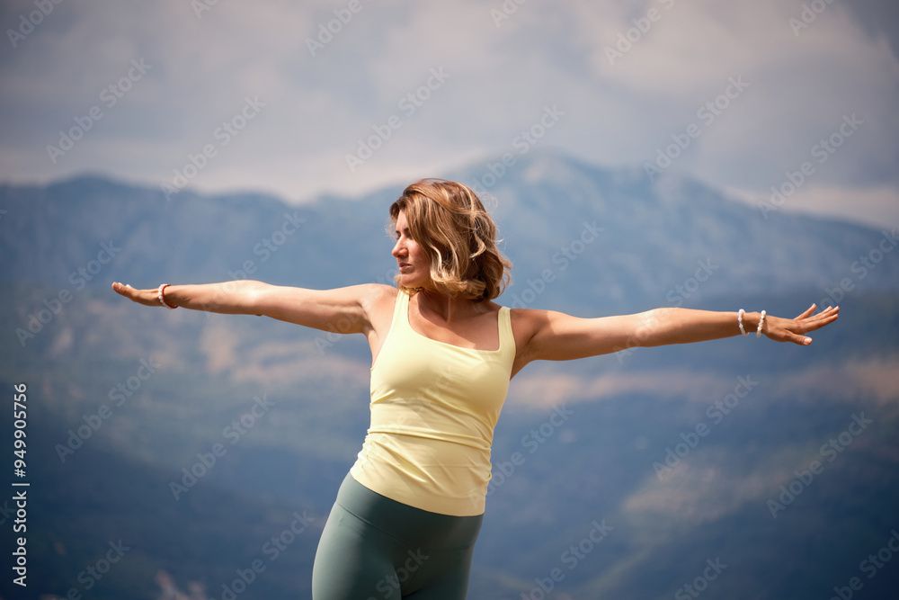 A woman is standing on top of a mountain with her arms outstretched.