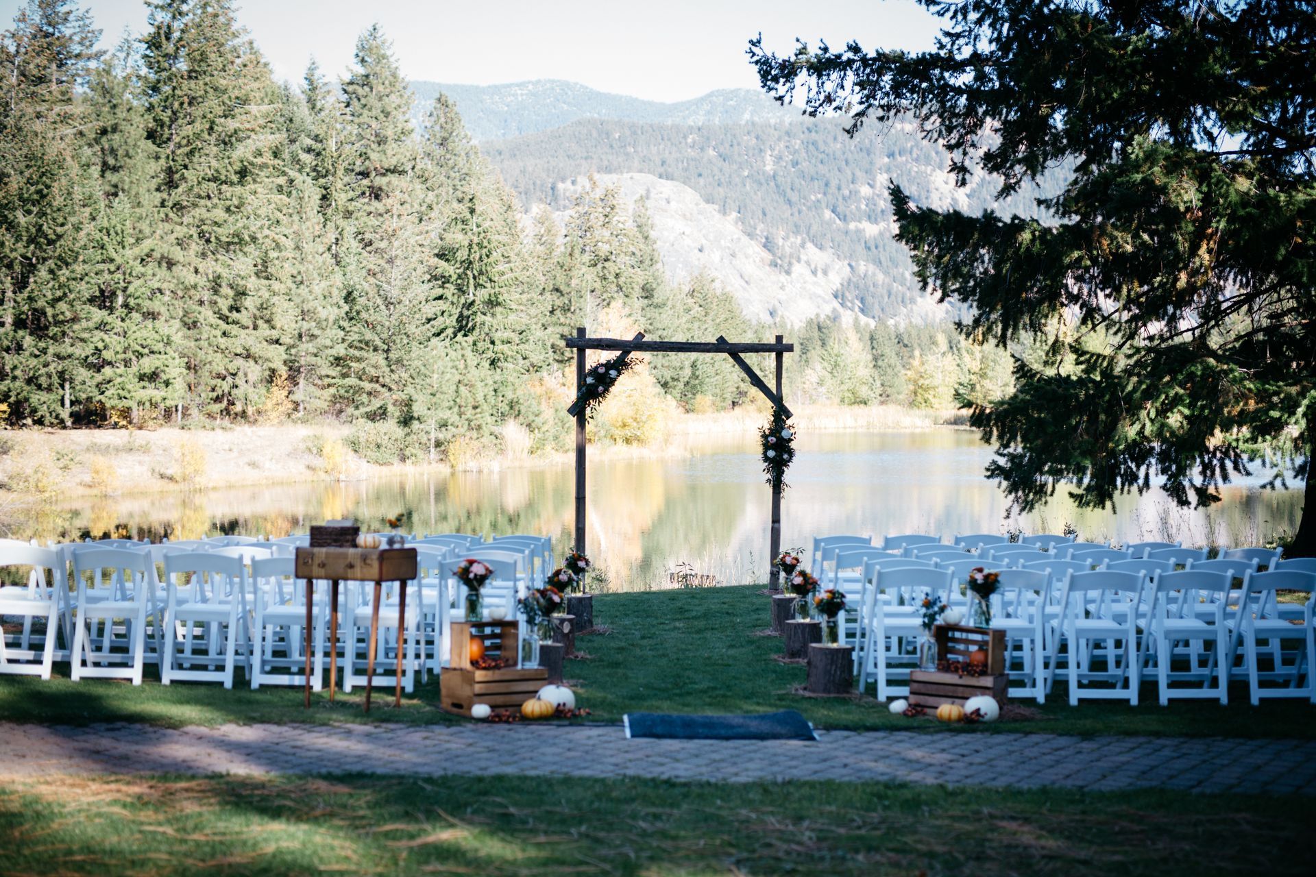 A wedding ceremony is taking place in front of a lake surrounded by trees.