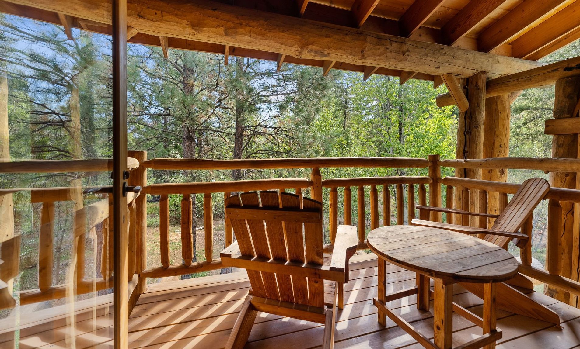 Wooden balcony with two chairs and a small table, overlooking a forest.