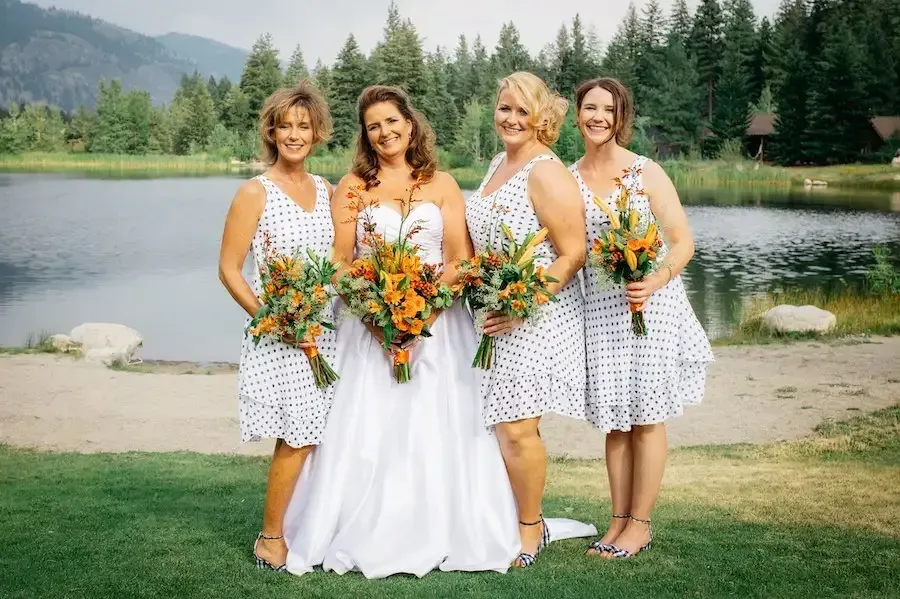A bride and her bridesmaids are posing for a picture in front of a lake.