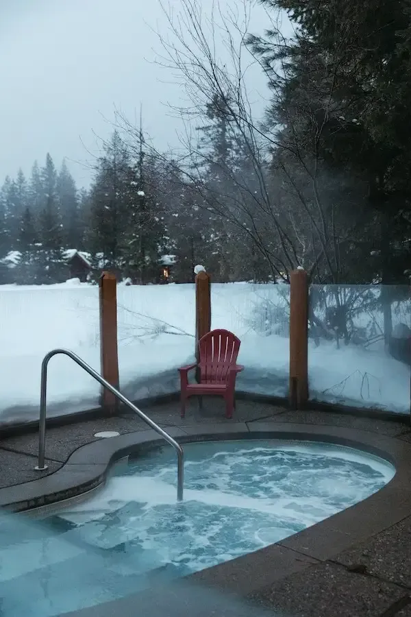 A hot tub surrounded by snow with a red chair in the background.