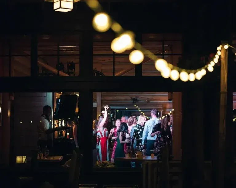 Party scene through a window: people dancing under string lights.