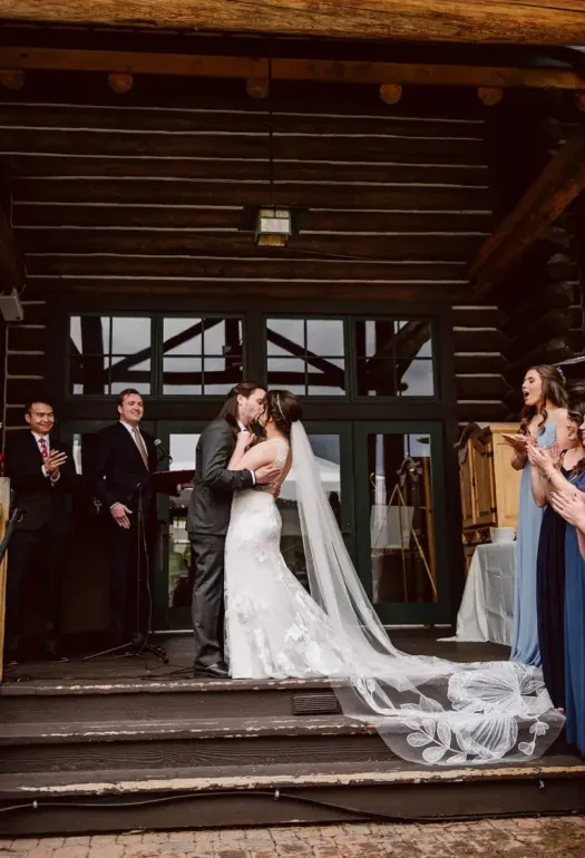 A bride and groom kissing in front of a wooden building.