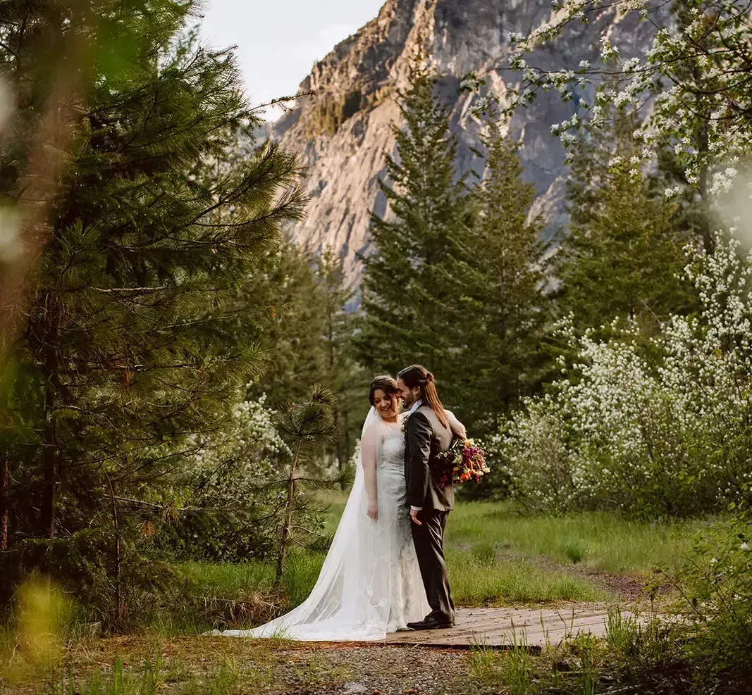 A bride and groom are posing for a picture in the woods.