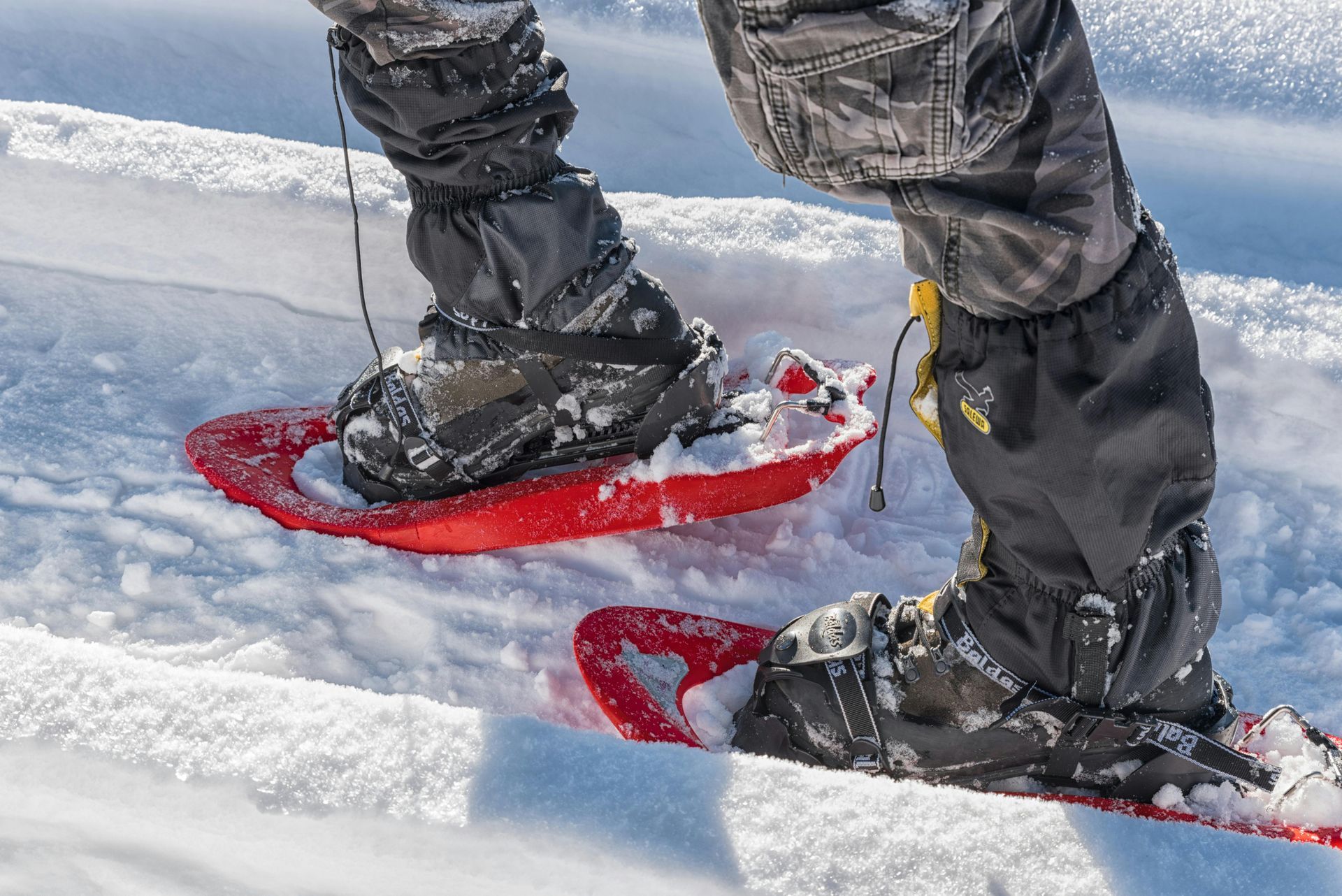 Person wearing black snow gaiters and snowshoes, standing in fresh snow.