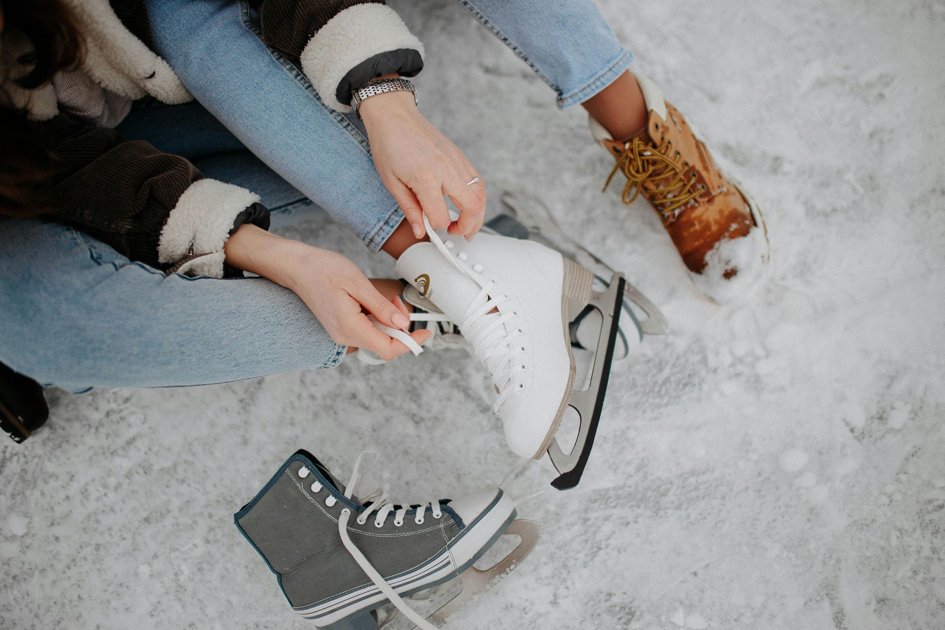 Person tying ice skate on snowy ground; other skate nearby.
