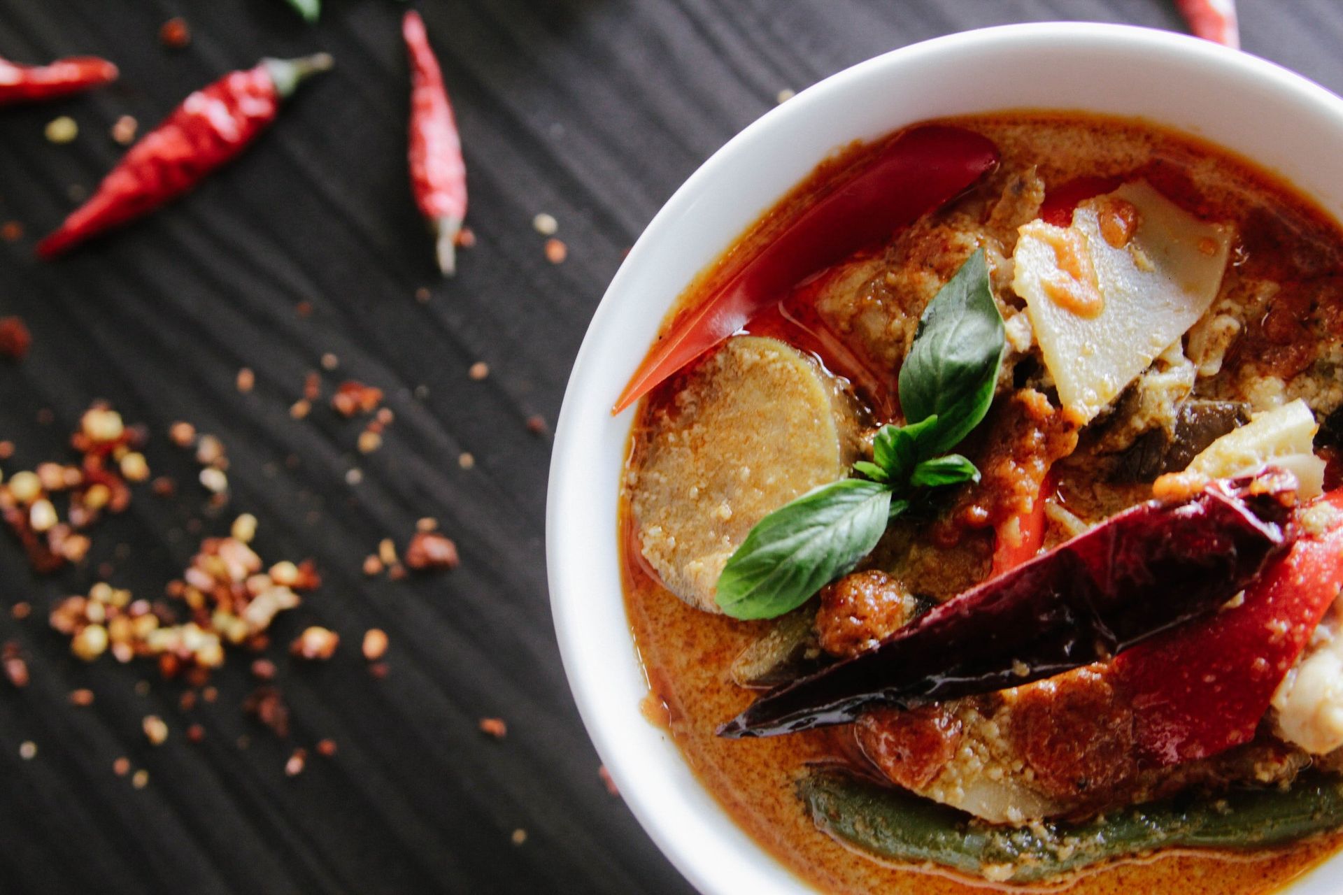 A bowl of soup with vegetables and chili peppers on a table.