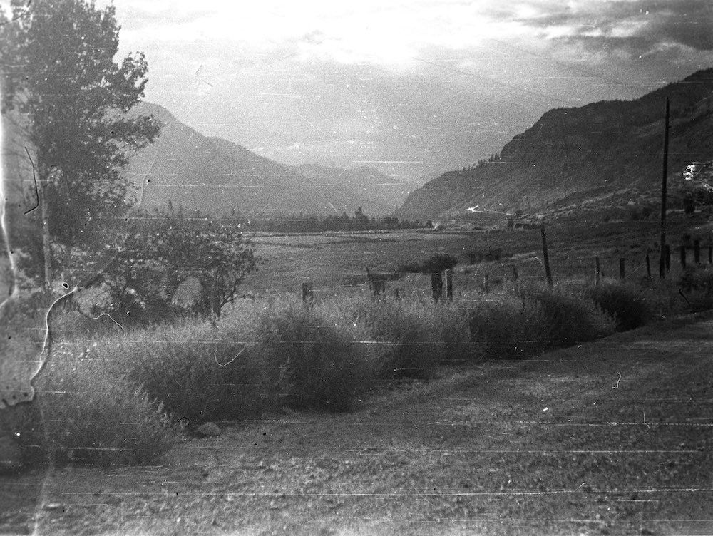 A black and white photo of a field with mountains in the background.